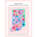 Indiana-shaped holographic sticker covered in colorful pressed flowers, displayed on a light pink background with the text 'INDIANA HOLOGRAPHIC STICKER' and a website URL.