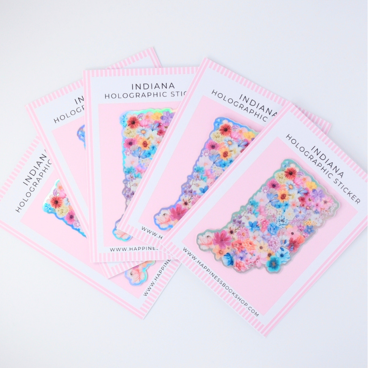 Five pink cards labeled 'INDIANA HOLOGRAPHIC STICKER' fanned out on a white background, each showing a colorful floral holographic sticker shaped like the state of Indiana.